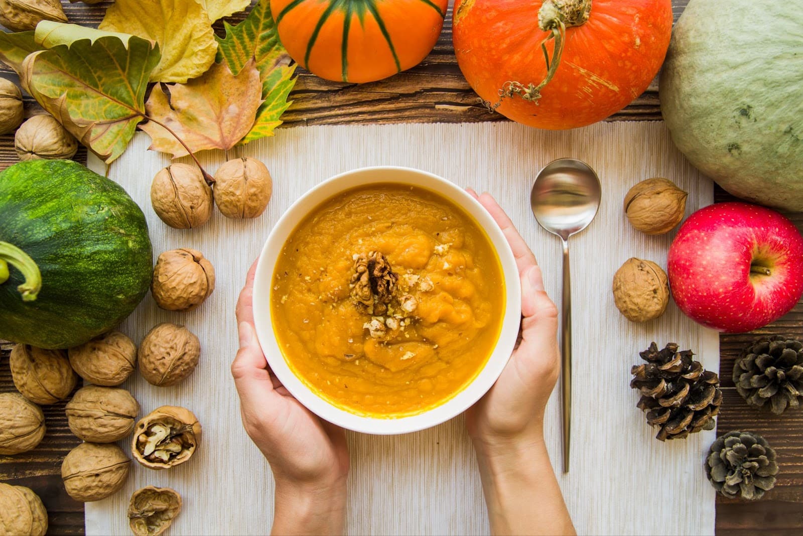 Top view of hands holding bowl of pumpkin soup with walnuts