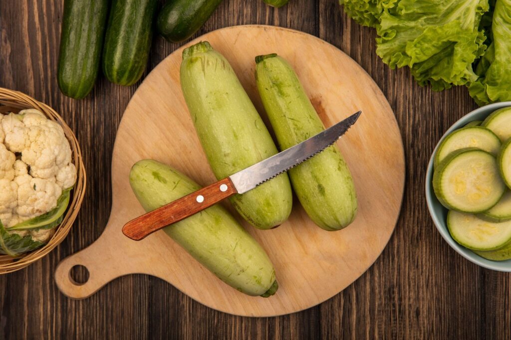 Top view of zucchinis on a wooden kitchen board with knife and cauliflower