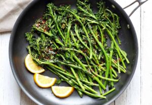 A skillet with sautéed broccolini, garlic, red pepper flakes, and lemon slices
