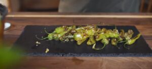 Charred shishito peppers laid out on a black slate board.
