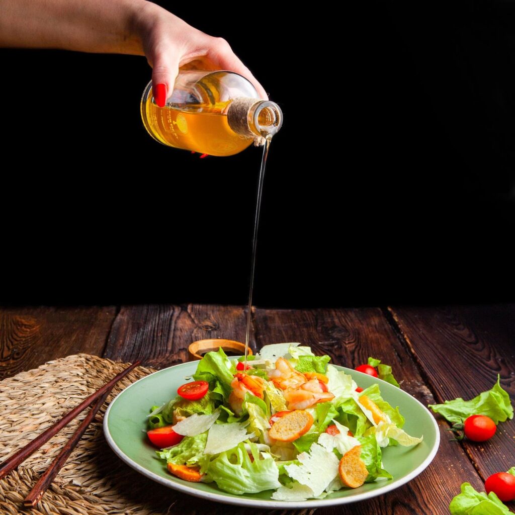 Woman pouring oil on delicious salad in plate